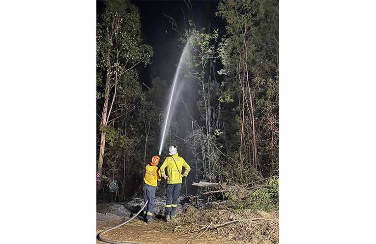 Firefighters Wayne Pade and Lachlan Pade extinguish a dead tree alight on the edge of a containment line. Photo: Ella Pade.